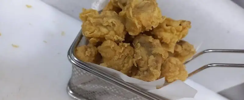 تصویری جذاب از پاپ کورن مرغ سوخاری طلایی و ترد، سرو شده در سبد فلزی شیک فست فود لاکچری، با طعمی بی‌نظیر و به یاد ماندنی.