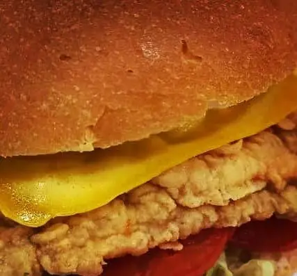 تصویری نزدیک از ساندویچ مرغ سوخاری ترد و لذیذ با پنیر ذوب شده و تازه، انتخابی عالی برای فست فود لاکچری و دوستداران غذای باکیفیت.