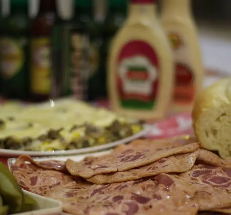 برش‌های کالباس با نان تازه، ترشی، و غذای اصلی فست فود لاکچری (شبیه لازانیا) در میز دورهمی با سس‌های متنوع آماده سرو است.