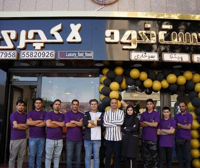 عکس از پرسنل فست فود لاکچری در مقابل تابلوی طلایی، ارائه دهنده بهترین پیتزا و سوخاری در شهر