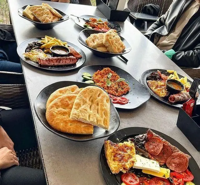 میز چیدمان شده صبحانه/برانچ کامل کافه رستوران سیتی تراس با انواع نان، املت، سوسیس، پنیر و دورچین‌های متنوع.