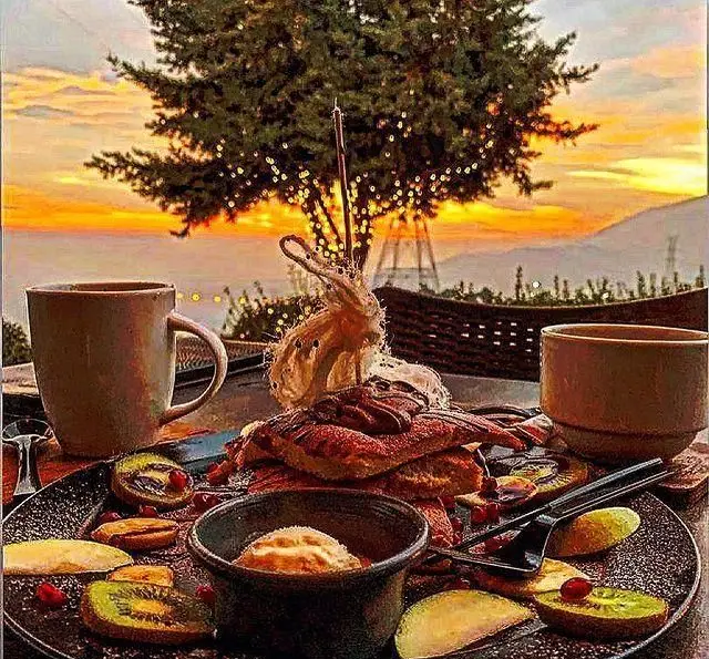 صبحانه لوکس کافه رستوران سیتی تراس با منظره خیره کننده غروب کوهستان و درختان نورانی؛ تجربه ای دلنشین در فضای باز.