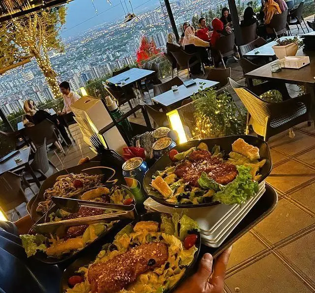 کافه رستوران سیتی تراس: منظره شبانه شهر از تراس، فضای لوکس و دلنشین، میزهای پر از مشتریان و سینی غذاهای آماده سرو.