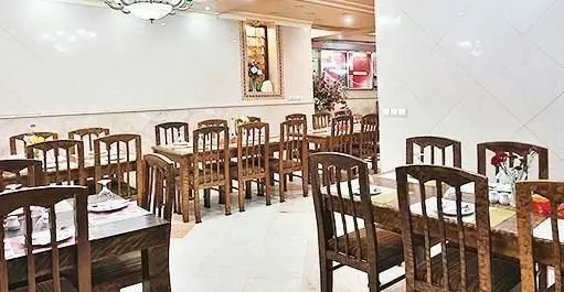 فضای داخلی رستوران ایرانی تواضع با چیدمان میز و صندلی‌های چوبی شیک و دکوراسیون سنتی، محیطی دلنشین برای صرف غذای ایرانی اصیل.