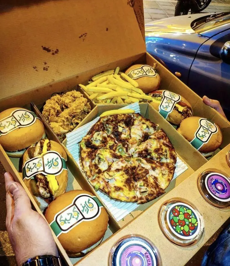جعبه بزرگ فست فود کاریز کوچیکه حاوی پیتزا، چندین برگر لذیذ، سیب زمینی سرخ کرده، مرغ سوخاری و سس‌های جذاب، آماده سرو.