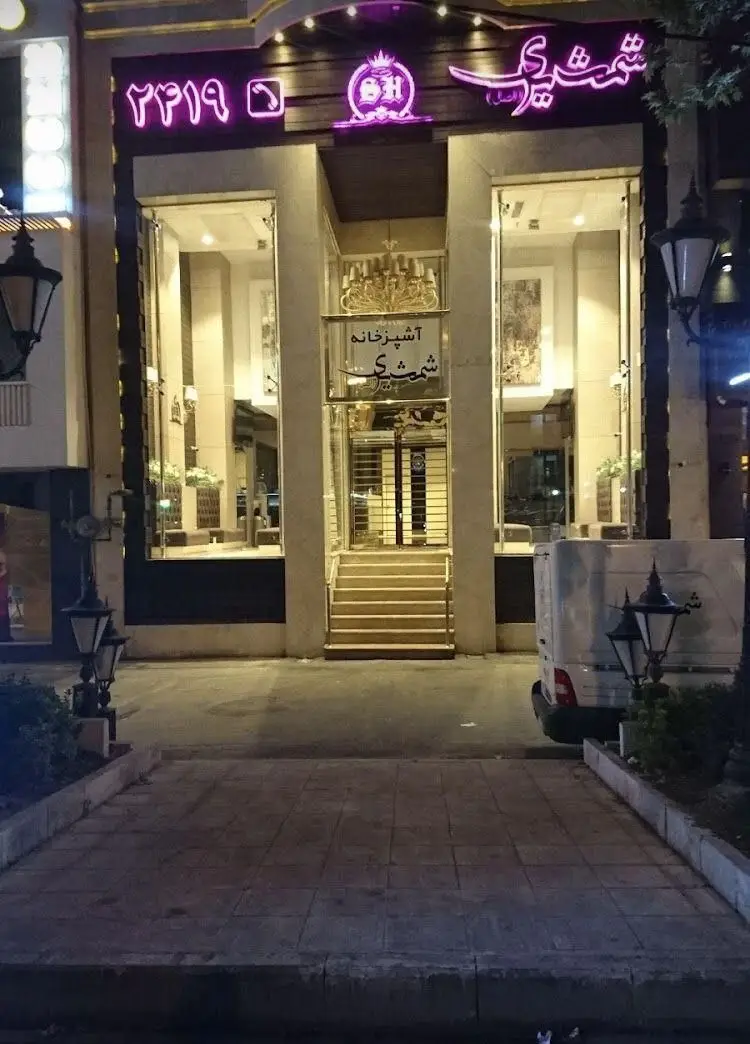 تصویر بیرونی رستوران شمشیری در شب، آشپزخانه معروف و لوکس غذاهای اصیل ایرانی با تابلو نئون و آدرس تماس.