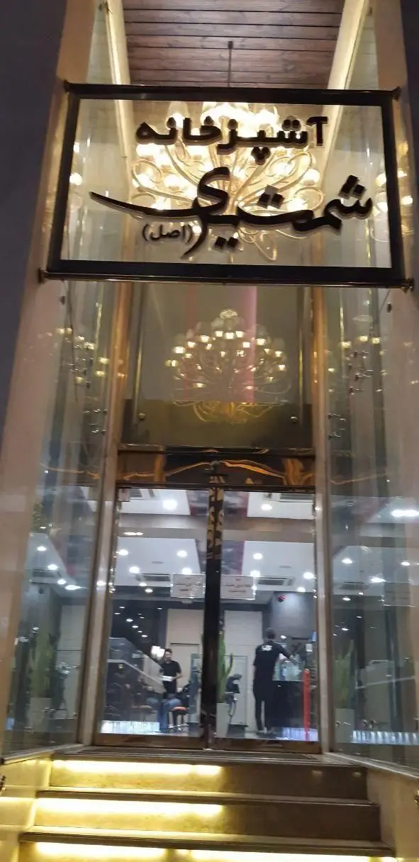 نمای ورودی مدرن و شیک رستوران آشپزخانه شمشیری (اصل) با تابلوی روشن و پله‌های نورانی. محیطی دلنشین برای پذیرایی.