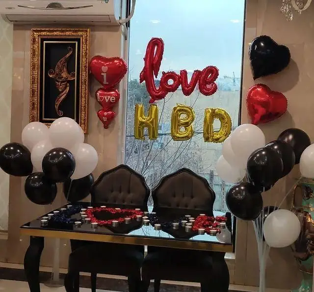 سفره خانه خیام: دکوراسیون جشن تولد یا سالگرد با بادکنک‌های Love و HBD، قلب‌های قرمز، شمع‌آرایی و میز دو نفره.