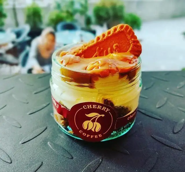 دسر شیشه ای کافه چری: لایه های کرمی، بیسکویت لوتوس و سس کارامل. تصویری اشتهاآور از محصولات کافه چری، مناسب کافه و کافی شاپ.