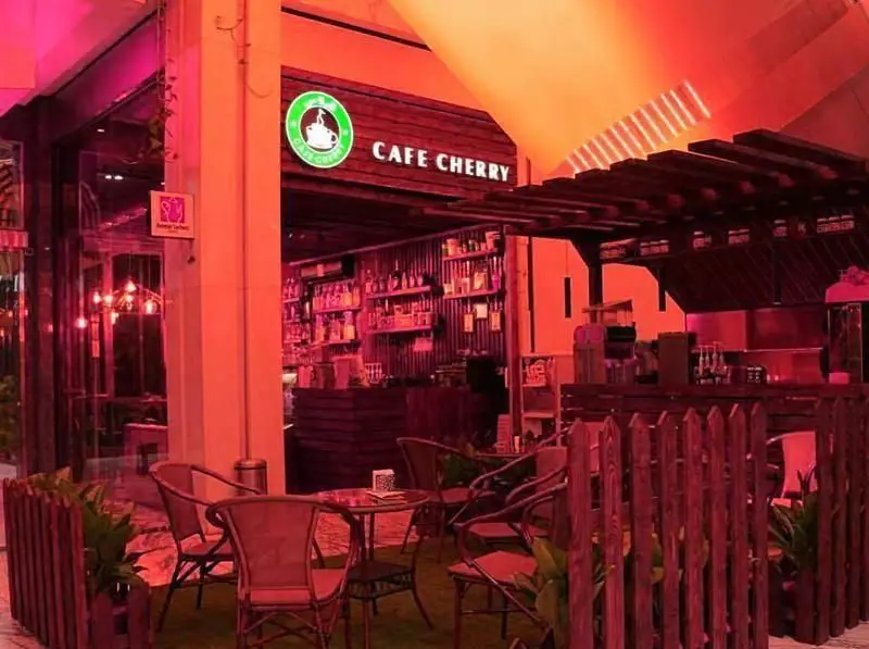 نمای ورودی کافه چری با تابلوی سبز، فضای بیرونی آرامش‌بخش، نورپردازی گرم، میز و صندلی‌های شیک و بار داخلی.