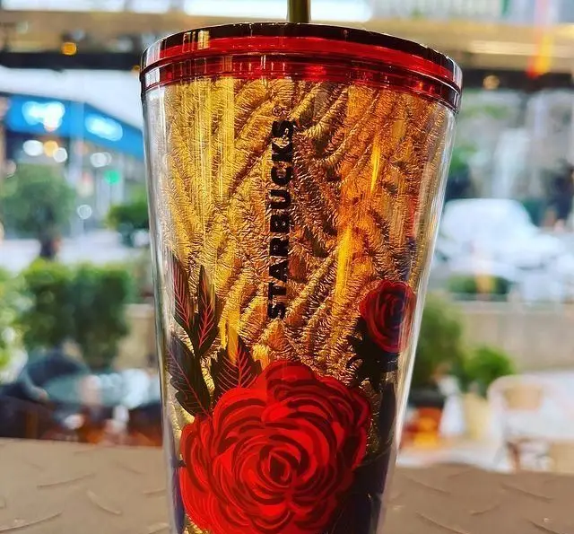 ماگ استارباکس طلایی با درب قرمز و طرح گل رز برجسته، ایده‌آل برای نوشیدن قهوه و چای در فضای دلپذیر کافه چری. کافه لاکچری.