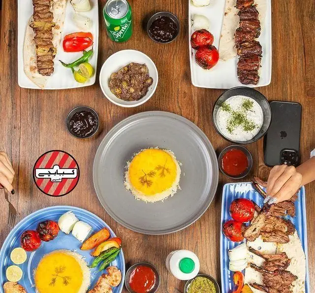 تصویری زیبا از میز پر از غذاهای لذیذ رستوران کبابچی آجودانیه، شامل کباب‌های کوبیده، جوجه، شیشلیک و ته دیگ زعفرانی.