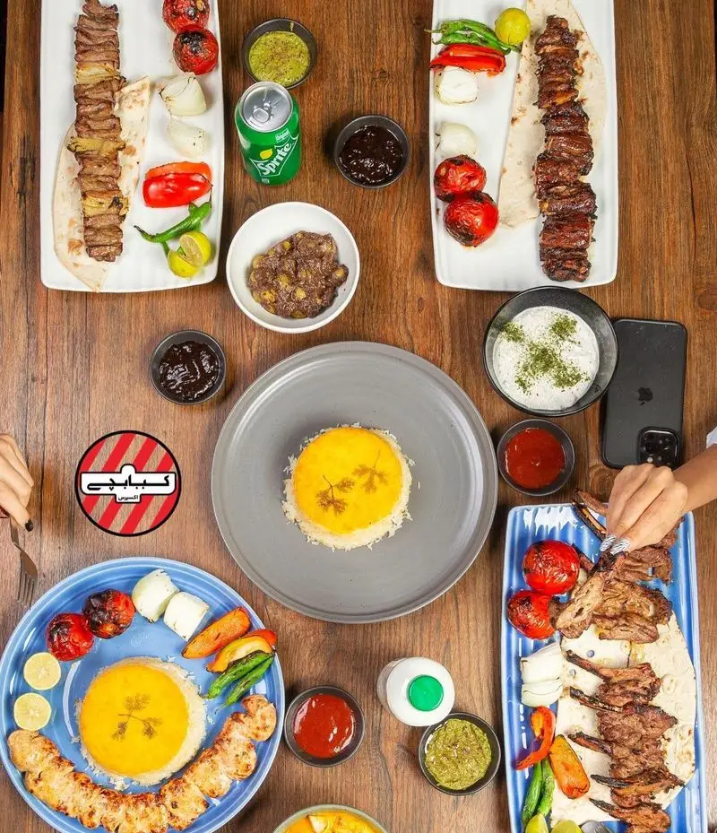 میز پر از انواع کباب‌های لذیذ ایرانی شامل جوجه، برگ و شیشلیک با پلو زعفرانی و مخلفات در رستوران کبابچی آجودانیه.