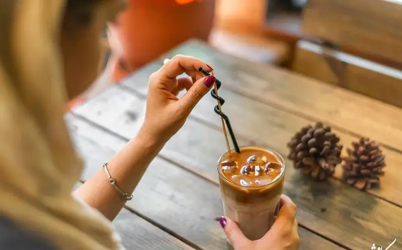 لذت نوشیدن آیس کافی خنک و گوارا در کافه رستوران کاویش، همراه با فضای دلنشین و میزهای چوبی. تجربه‌ای بی‌نظیر.