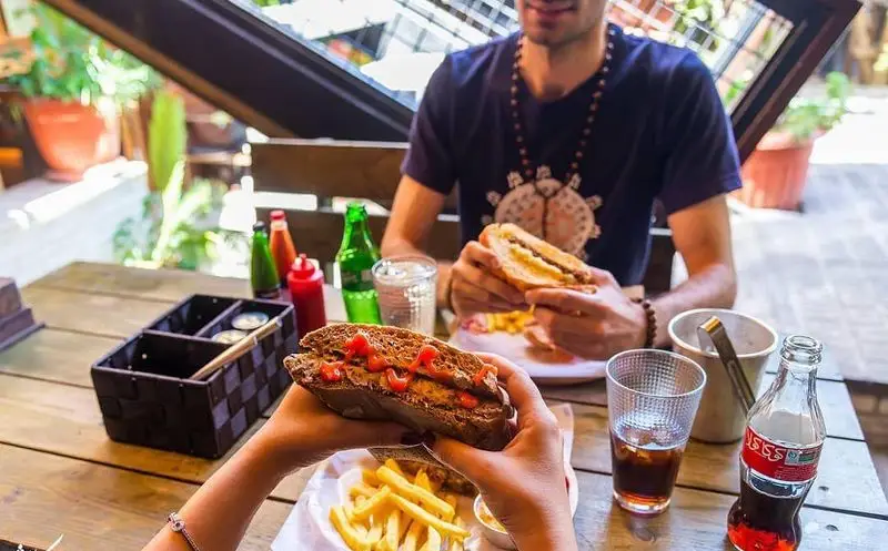 زوجی در کافه رستوران کاویش از ساندویچ‌های خوشمزه، سیب‌زمینی سرخ‌کرده و نوشیدنی‌های خنک در فضای دلنشین و باز لذت می‌برند.