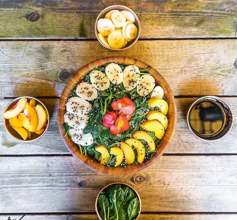 کاسه اسموتی سالم و رنگارنگ کافه رستوران کاویش با موز، هلو و اسفناج تازه، ایده‌آل برای صبحانه یا میان‌وعده مقوی.