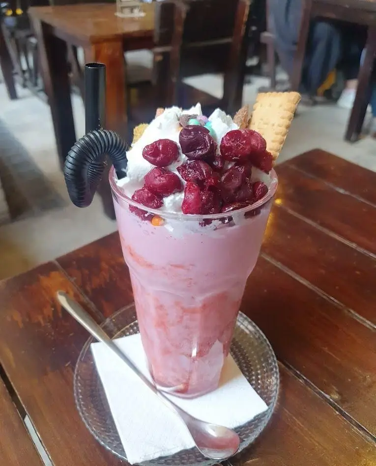 میلکشیک صورتی و دلپذیر با خامه، توت‌های قرمز و تزئین بیسکویت، نوشیدنی خنک در کافه رستوران کاویش برای لحظاتی شیرین و آرامش‌بخش.
