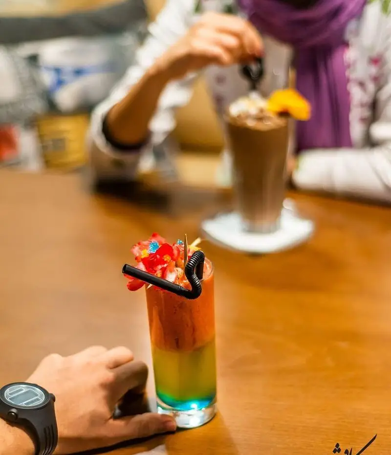 مشتریان در کافه رستوران کاویش از نوشیدنی‌های رنگارنگ میوه‌ای و دسرهای لذیذ لذت می‌برند، تجربه‌ای دلنشین در محیطی آرام.