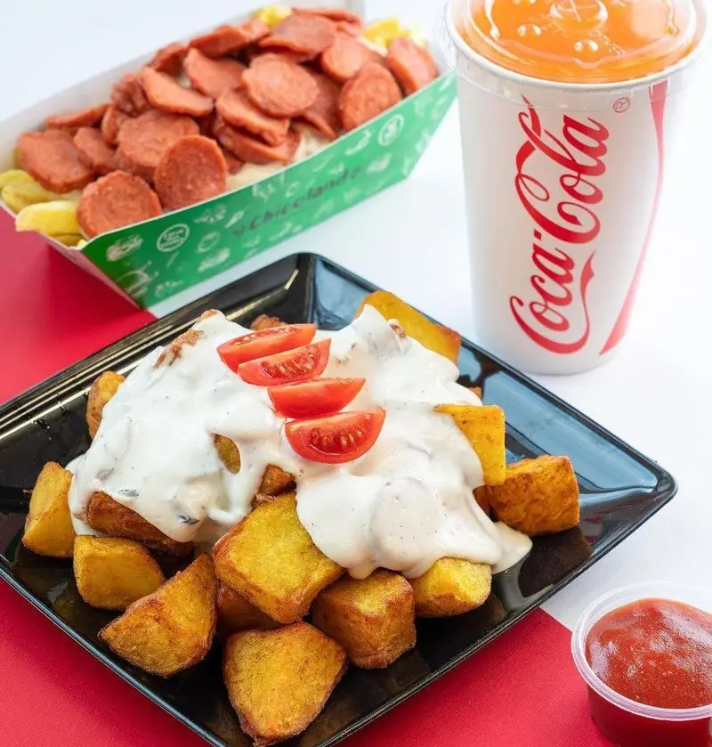 سفارش فست فود چیکولند: بشقاب سیب‌زمینی سرخ شده با سس مخصوص و گوجه، ظرف سیب‌زمینی و سوسیس، همراه با نوشابه کوکاکولا و کچاپ.