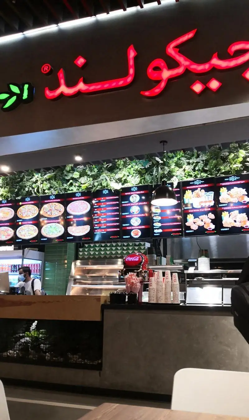 نمایی از فضای داخلی فست فود چیکولند با تابلوی نئونی برند، منوهای دیجیتال پیتزا، مرغ سوخاری و پیشخوان سفارش غذا.