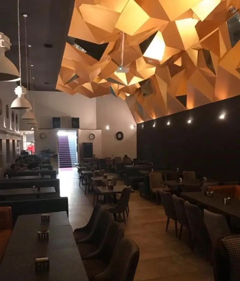 نمایی از فضای داخلی رستوران فرنگی ده و ده، با طراحی سقف هندسی مدرن و منحصر به فرد طلایی، و چیدمان شیک میز و صندلی.