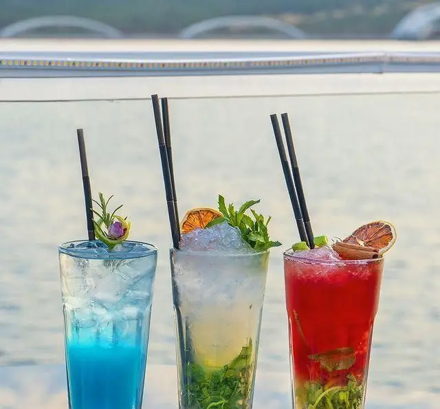 نوشیدنی‌های خنک و متنوع در کشتی رستوران رویال لانژ: سه کوکتل جذاب آبی، سبز و قرمز با یخ و تزئین میوه و سبزیجات تازه.