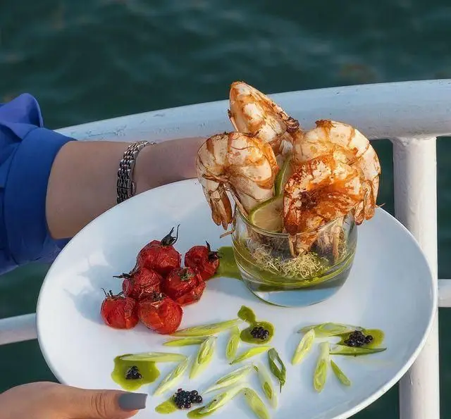 سرو بی‌نظیر میگوی کبابی، گوجه و پیازچه در کشتی رستوران رویال لانژ، لذت غذای دریایی لوکس با منظره‌ای خاص.