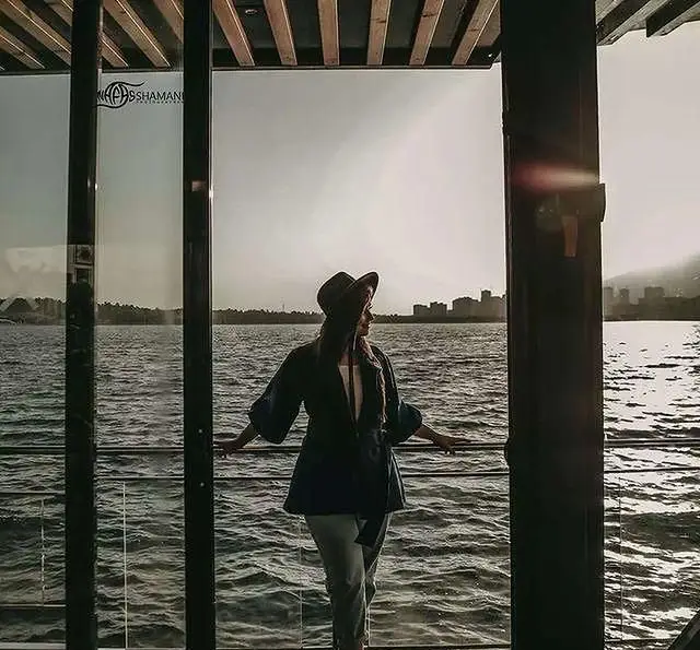 زنی با کلاه در کشتی رستوران رویال لانژ، مشرف به منظره‌ خیره‌کننده دریا و افق شهر، تجربه‌ای لوکس و آرامبخش بر روی آب.