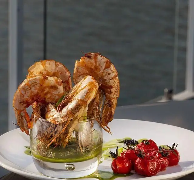 تجربه غذای لوکس دریایی: میگوهای کبابی تازه و خوش‌طعم در کنار گوجه گیلاسی، سرو شده در کشتی رستوران رویال لانژ با منظره دیدنی.