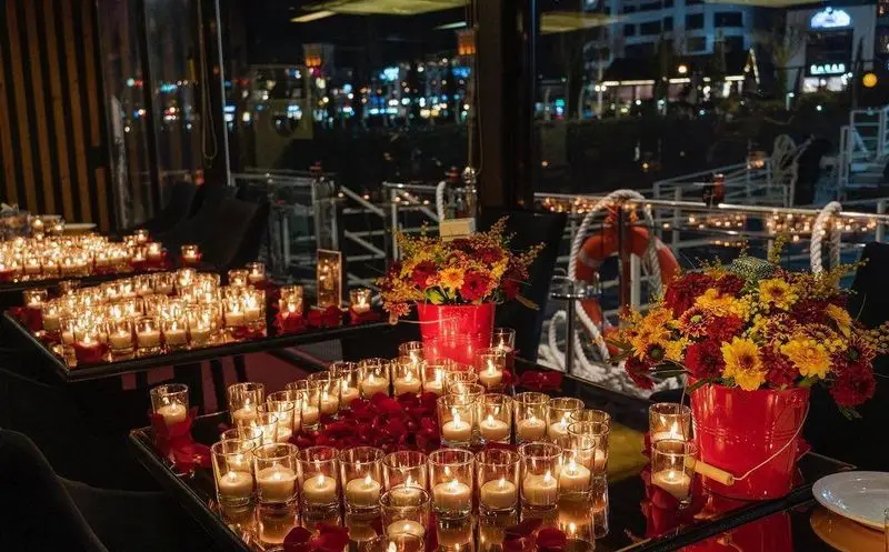 دکوراسیون رمانتیک و لوکس کشتی رستوران رویال لانژ در شب با نور شمع‌های فراوان، گل‌های زیبا و گلبرگ‌های رز برای یک شام خاص.