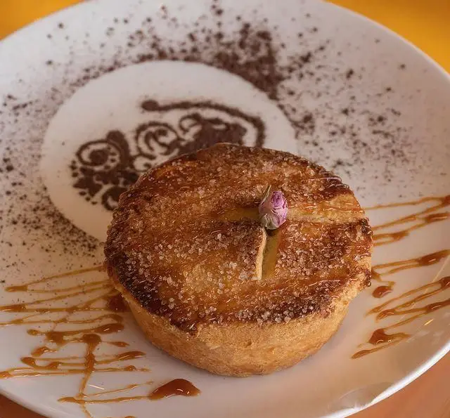 دسر پای تازه پخته شده طلایی و خوش طعم با شکر کریستالی، غنچه گل رز ظریف، سس کارامل و طراحی پودر کاکائو در کشتی رستوران رویال لانژ.