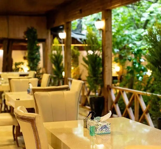 محیط دنج و زیبای کبابسرای شب زدگان با میز و صندلی‌های شیک و راحت در فضای سبز، ایده‌آل برای شب‌نشینی و صرف کباب.