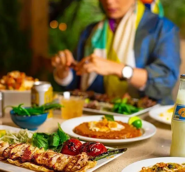 میز غذای پرشکوه کبابسرای شب زدگان: جوجه کباب، گوجه، دوغ و سبزیجات. تجربه طعم بی‌نظیر غذای اصیل ایرانی در محیطی دلنشین.