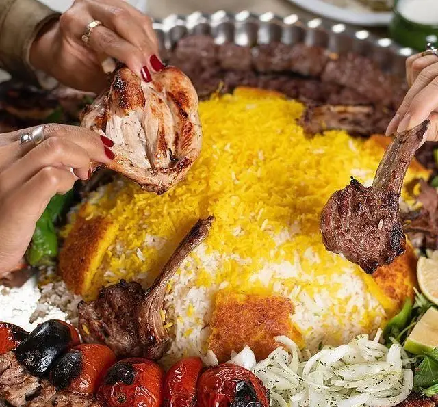 تصویری از سفره دلپذیر کبابسرای شب زدگان شامل چلوکباب، جوجه، شیشلیک، گوجه، پیاز و برنج زعفرانی؛ غذای اصیل ایرانی.