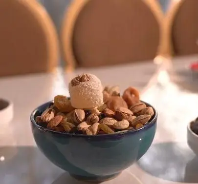 پذیرایی سنتی با کاسه‌ای از آجیل و شیرینی باسلوق در کبابسرای شب زدگان، نشان‌دهنده مهمان‌نوازی و فضای دلنشین رستوران.