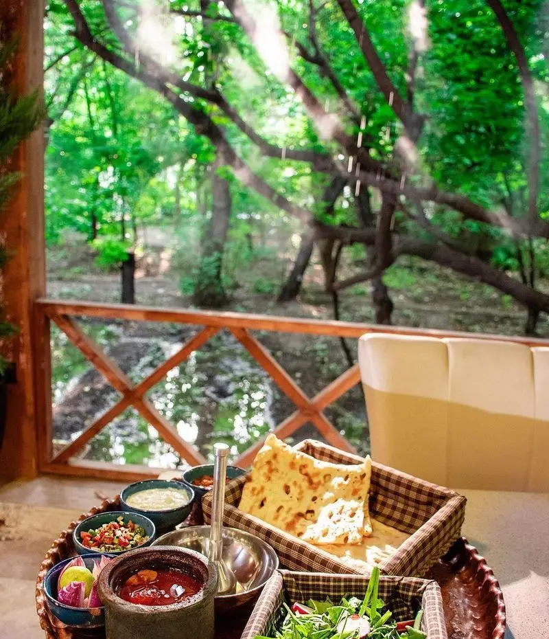 کبابسرای شب زدگان: یک وعده غذایی دلنشین با کباب، نان داغ، سالاد و مخلفات در بالکن رو به منظره‌ای بی‌نظیر از طبیعت.