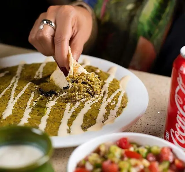 لذت تجربه طعم اصیل غذای خاورمیانه‌ای در کبابسرای شب زدگان: دست در حال دیپ کردن نان در دیپ سبز لذیذ با سس مخصوص.