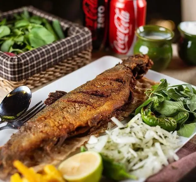 ماهی قزل آلای سرخ شده خوشمزه با سبزی تازه، پیاز، لیمو، فلفل و سیب زمینی از کبابسرای شب زدگان، یک غذای اصیل ایرانی.