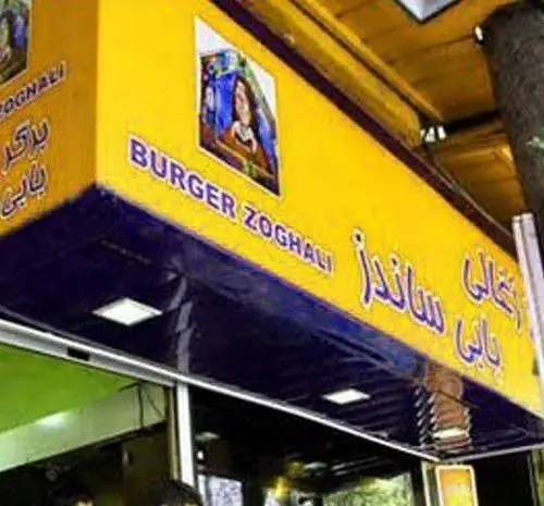 تابلوی مغازه بابی ساندز با فونت بزرگ، نمایش‌دهنده تخصص در برگر و ساندویچ ذغالی. جلوه‌ای روشن و دعوت‌کننده برای مشتریان فست فود.