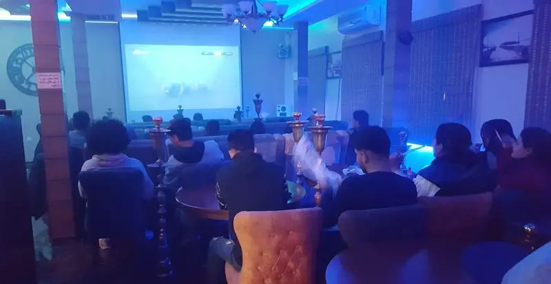 کافه عربی جمیرا: مشتریان جوان در فضای دنج و آبی کافه، سرگرم تماشای پروژکتور و لذت بردن از قلیان با دوستان.