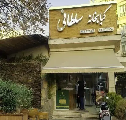 نمایی از نمای بیرونی کبابی سلطانی شعبه ۲ در تهران، با تابلوی روشن، سایبان بژ و ورودی جذاب برای مشتریان.