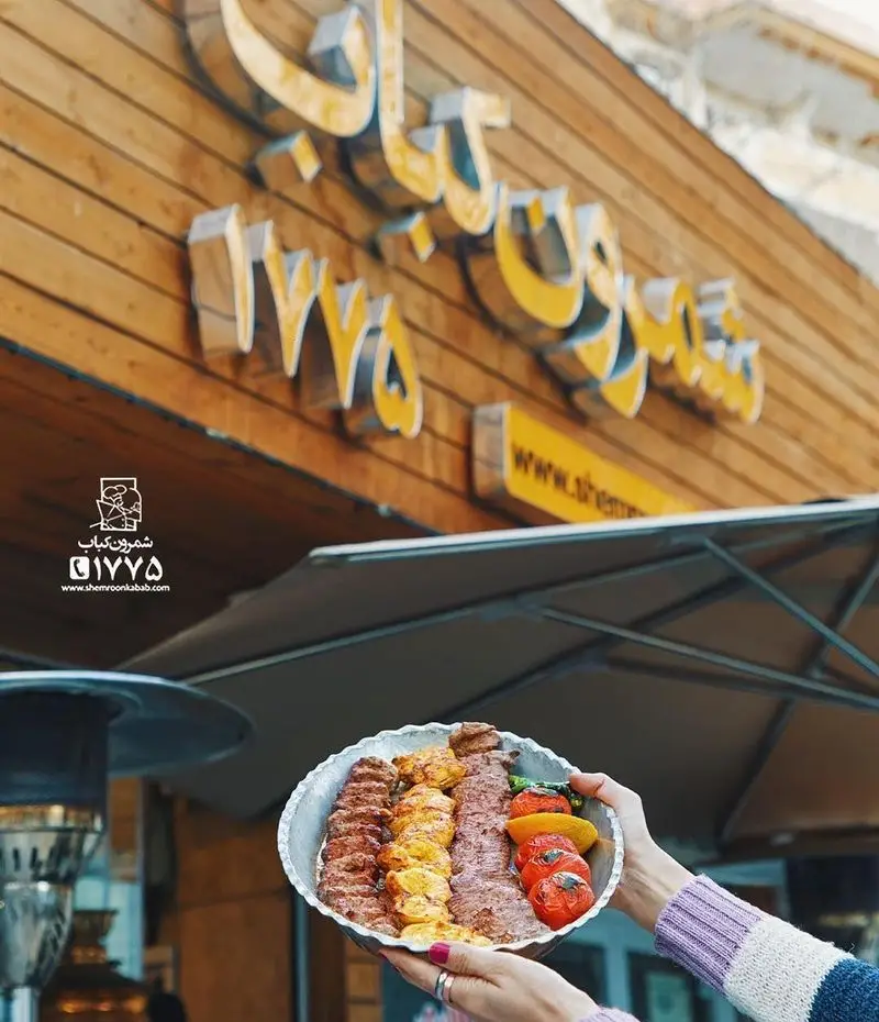 یک بشقاب کباب‌های تازه و لذیذ ایرانی از شمرون کباب ۱۲۷۵، شامل کوبیده، جوجه و برگ با گوجه کبابی، در مقابل نمای چوبی رستوران.