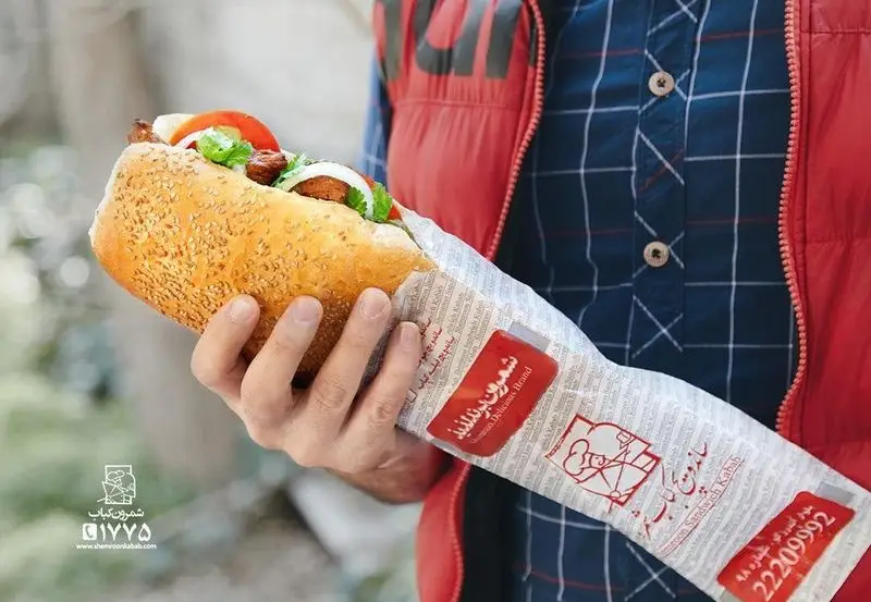 ساندویچ کباب بزرگ و لذیذ شمرون کباب با نان کنجدی تازه، گوشت کباب، گوجه و پیاز در بسته‌بندی برند Shemroon Kebab.