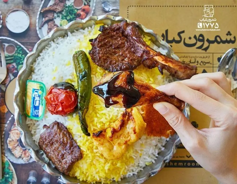 شمرون کباب: سینی چلوکباب مجلل با شیشلیک، جوجه کباب و کباب گوشت، گوجه و فلفل کبابی، کره. دستی روی جوجه کباب سس می‌ریزد.