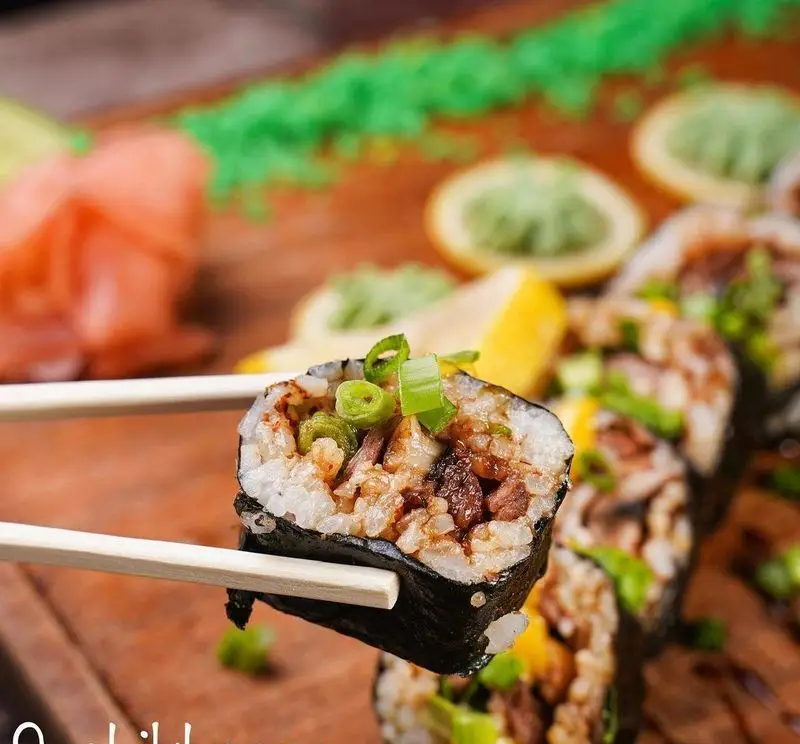 رول سوشی با مغز گوشت و برنج، تزئین شده با پیازچه تازه، آماده برای سرو. تجربه طعم بی نظیر در سوشی خونه قیطریه.