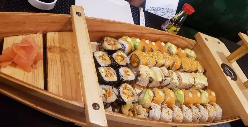 سینی بزرگ چوبی سوشی با انواع رول‌های ماکی و اوراماکی رنگارنگ، شامل سوشی میگو، سالمون و سبزیجات، به همراه زنجبیل و سس سویا در سوشی خونه قیطریه.