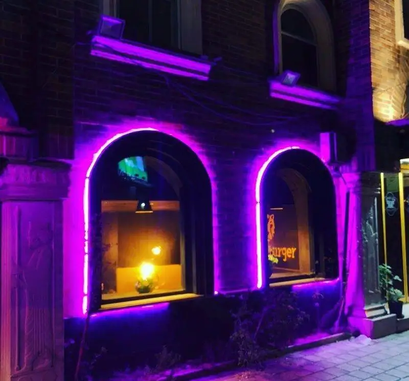 نمای شیک و مدرن رستوران نچرال برگر در شب با نورپردازی خیره‌کننده نئون بنفش، پنجره‌های قوسی و معماری جذاب.