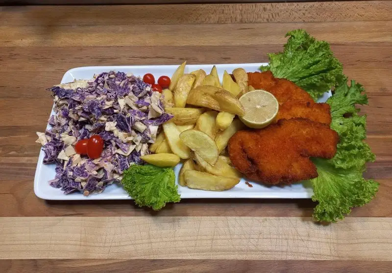 عکس نزدیک از بشقاب لذیذ ممل برگر با دو تکه فیله مرغ سوخاری طلایی، سیب زمینی سرخ کرده وجز، سالاد کلم بنفش و تازه، همراه با لیمو و گوجه گیلاسی.