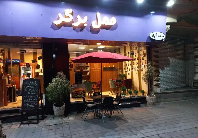 ممل برگر، فست فود محبوب یافت آباد با نمای شیک، تابلوی روشن، فضای نشستن باز با چتر قرمز و منوی متنوع برگر و نوشیدنی.
