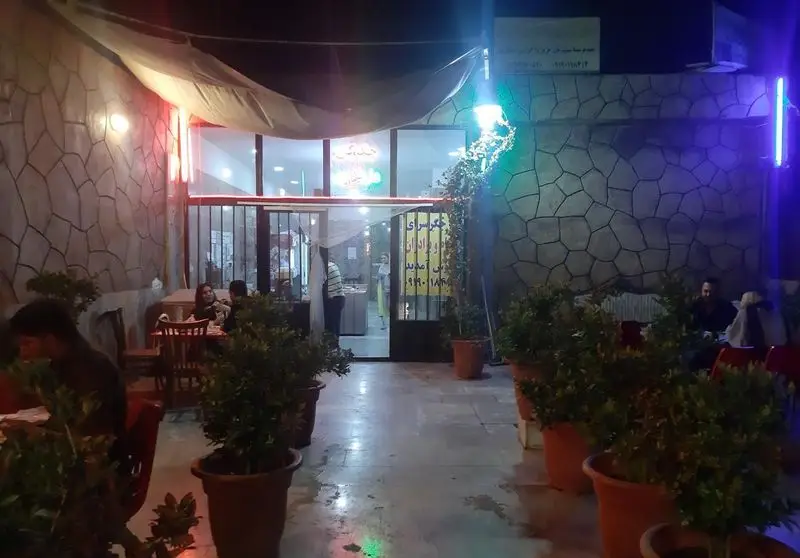 نمایی شبانه از فضای باز جگرسرای بهنام و برادران با مشتریان در حال غذا خوردن، مناسب برای تجربه یک غذای لذیذ ایرانی.